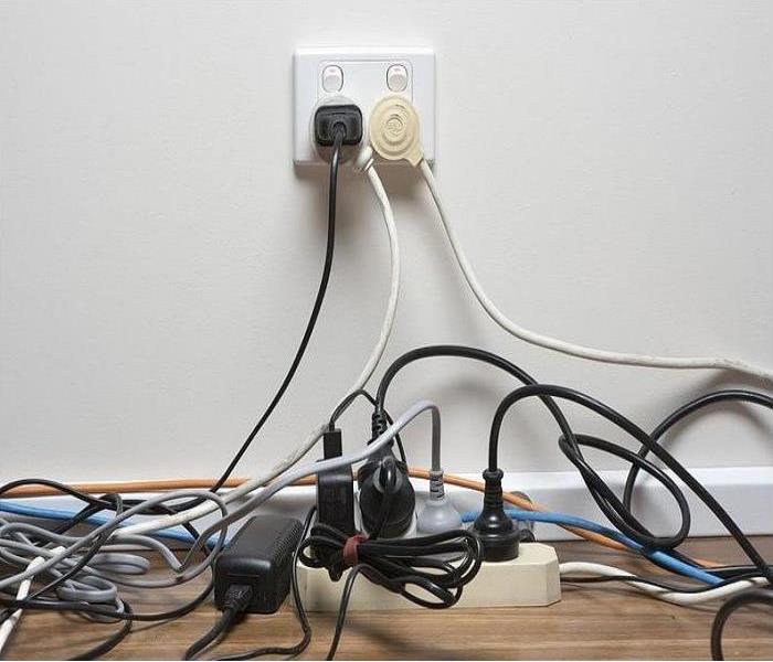A surge protector is overloaded by four extension cords inserted into the sockets, which is plugged into two wall outlets.