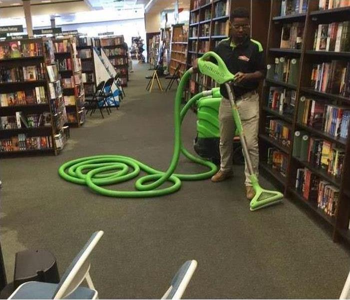 The Technician uses a steam cleaner to clean the wet carpet in a library.