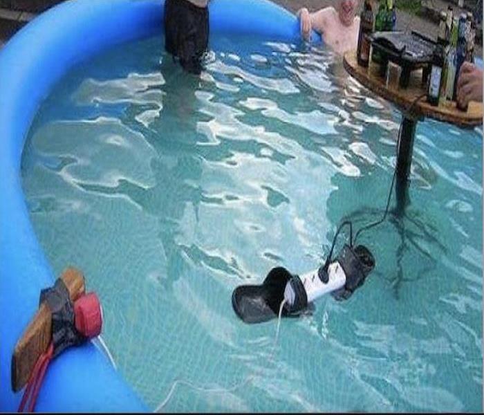Two men are in a pool, and they connected an electric cord to the outlet and placed it on top of the water.
