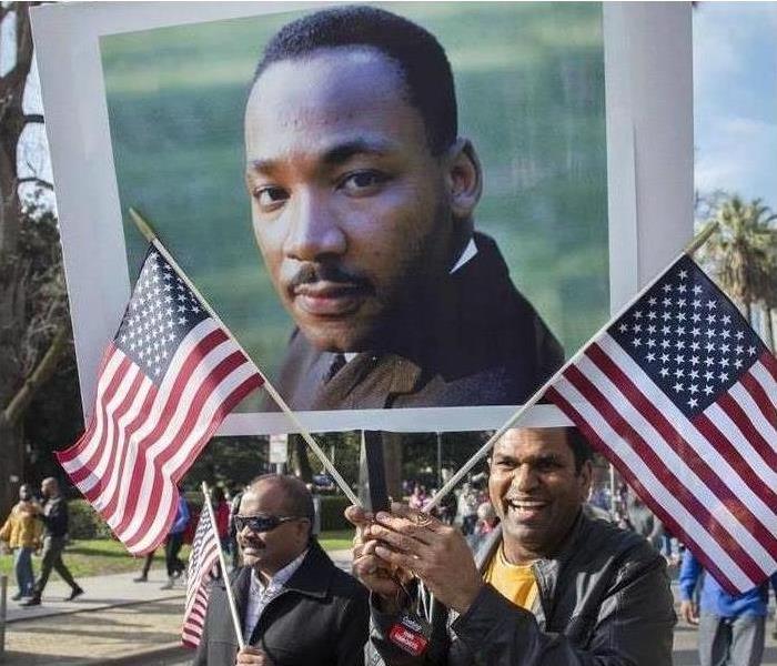 African Americans wave the American flag in a parade, and they have a poster of Martin Luther King on display.